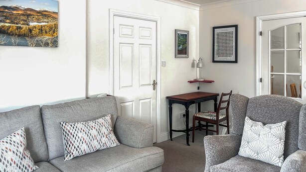 Ein Wohnzimmer mit grauem Sofa, einem passenden Sessel, einem kleinen Holztisch und einem gerahmten Bild an der Wand.