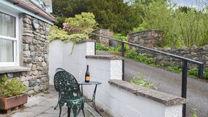 A stone wall with a metal railing, a green metal chair, and a table with a bottle and glass.