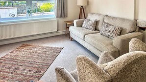 A living room with a sofa, armchairs, a lamp, a painting, and a view through a window.