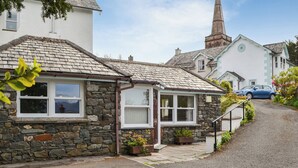 A stone cottage with a pitched roof, a small porch, and a car parked on the street.