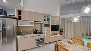 A modern kitchen with built-in appliances, a dining area with a table set for two, and a living room with a TV and seating. - Maui Beach Residence (Tamandaré)