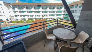 A balcony with a view of a swimming pool and a hotel building in the background. - Maui Beach Residence (Tamandaré)