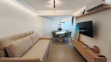 Una sala de estar moderna con un sofá, una zona de comedor con una mesa y sillas, y un televisor montado.