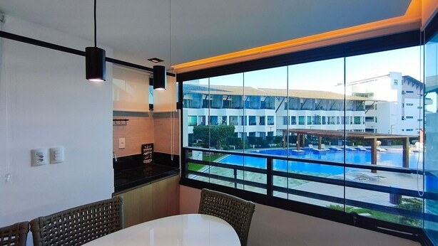 A room with a large window overlooking a swimming pool and a building complex. - Maui Beach Residence (Tamandaré)