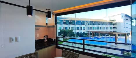 Una habitación con un amplio ventanal con vistas a una piscina y un conjunto de edificios.