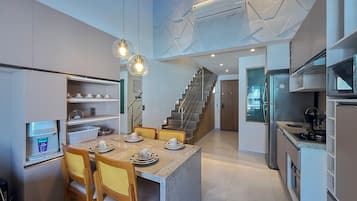 A modern kitchen with a dining area, built-in shelves, a refrigerator, and a staircase leading to another level.
