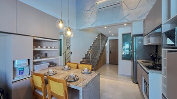 Una cocina moderna con comedor, estantes empotrados, refrigerador y una escalera que sube a otro nivel.