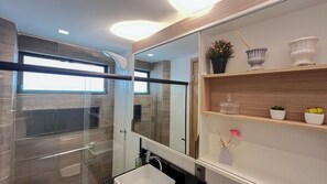 Ein modernes Badezimmer mit Duschkabine aus Glas, einem weißen Waschbecken und einem Spiegel über einem hölzernen Ablagebrett mit Dekorationen.