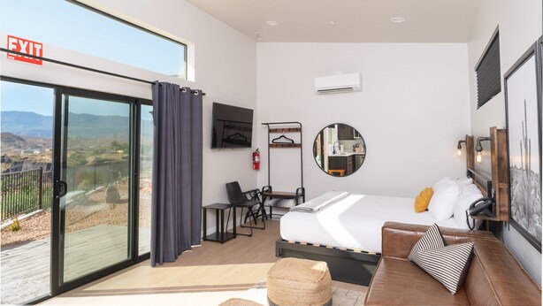 Una habitación de hotel moderna con una cama, una zona de estar, un escritorio y un gran ventanal con vistas panorámicas.