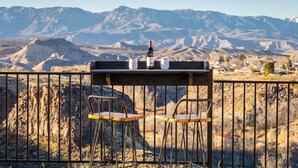 Una mesa con dos sillas y una botella de vino, con montañas al fondo.
