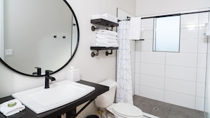 A modern bathroom with a large round mirror, a white sink, a black countertop, a toilet, and a shower area with a glass door. - Incredible View #5 at The Dwellings (La Verkin)