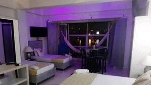 Ein modernes Hotelzimmer mit einem Bett, einem Schreibtisch und einem Sessel. Ein Fenster mit Vorhängen bietet einen Blick auf die beleuchtete Stadt bei Nacht.