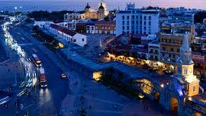 Eine Stadtansicht im Abenddämmerung mit beleuchteten Gebäuden und einer belebten Straße.