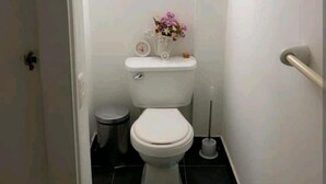 Ein kleines, schmales Badezimmer mit Toilette, Mülleimer und Toilettenbürste.