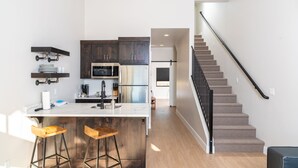 Una cocina moderna con armarios oscuros, un refrigerador de acero inoxidable y una barra con taburetes.