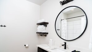 Ein modernes Badezimmer mit Toilette in Weiß, einem schwarzen Waschbecken, einem Spiegel und einem Handtuchhalter.