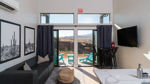 Ein modernes Hotelzimmer mit einer großen Glasschiebetür, die auf eine Außenpatio mit grünen Möbeln und schöner Aussicht führt.