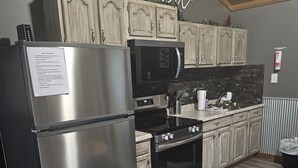 Une cuisine équipée d’un réfrigérateur en acier inoxydable, d’un four à micro-ondes, d’un four traditionnel et de meubles de rangement en bois.