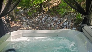 Un bain à remous doté d’un panneau de commande, entouré d’une terrasse en bois et intégré dans un paysage naturel.