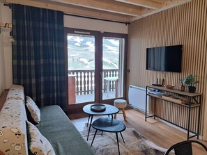 Una sala de estar con sofá, una mesita, un televisor y un balcón con vistas al exterior.