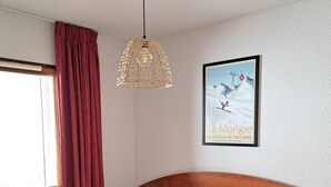 Uma cama bem arrumada com roupa de cama branca, cabeceira de madeira, luminária pendente e um quadro na parede.