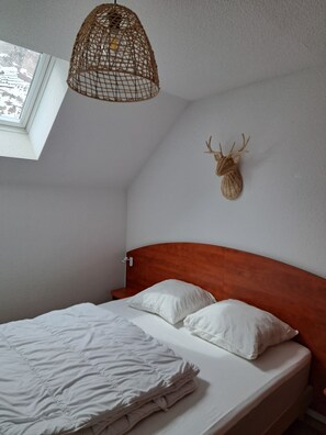 A bedroom with a wooden headboard, a bed with white bedding, a woven light fixture, and a mounted deer head on the wall.