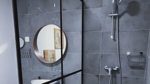 Un baño moderno con cabina de ducha de vidrio, un espejo redondo, tocador de madera y suelo de baldosas.