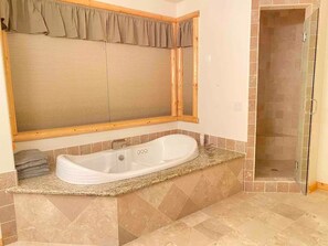 Ein Badezimmer mit einer freistehenden Badewanne, einer gläsernen Dusche und einem großen Spiegel mit Holzrahmen.