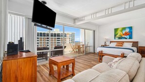 Et moderne hotelværelse med balkon, en stor seng, en sofa, et fjernsyn og et skrivebord.