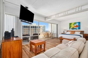 A modern hotel room with a balcony, a large bed, a sofa, a TV, and a desk.