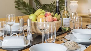 Mesa de comedor puesta con platos, vasos, un cuenco de fruta, una botella de vino y una lámpara.