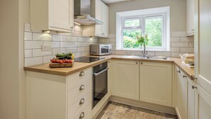 Una cocina moderna con armarios blancos, horno empotrado, microondas y ventana con vistas a zonas verdes.