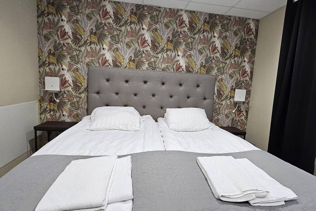 A neatly made bed with white linens, a grey textured bedspread, and two folded white towels.