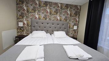 Een netjes opgemaakt bed met witte lakens, een grijs bedspreide en twee gevouwen witte handdoeken.