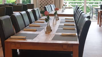 Une longue table à manger, entourée de chaises en cuir noir, est dressée avec soin : chaque place est mise et de petits vases décorés de fleurs y sont disposés.