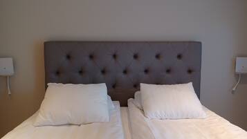A double bed with a tufted headboard, white bedding, and two bedside tables with wall-mounted lamps.