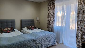 A hotel room with two beds, a large window with sheer curtains, and a light-colored wall.