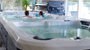 A hot tub with two people in it, surrounded by windows and a stack of luggage. - Hotell Solstickan Mellbystrand (Mellbystrand)
