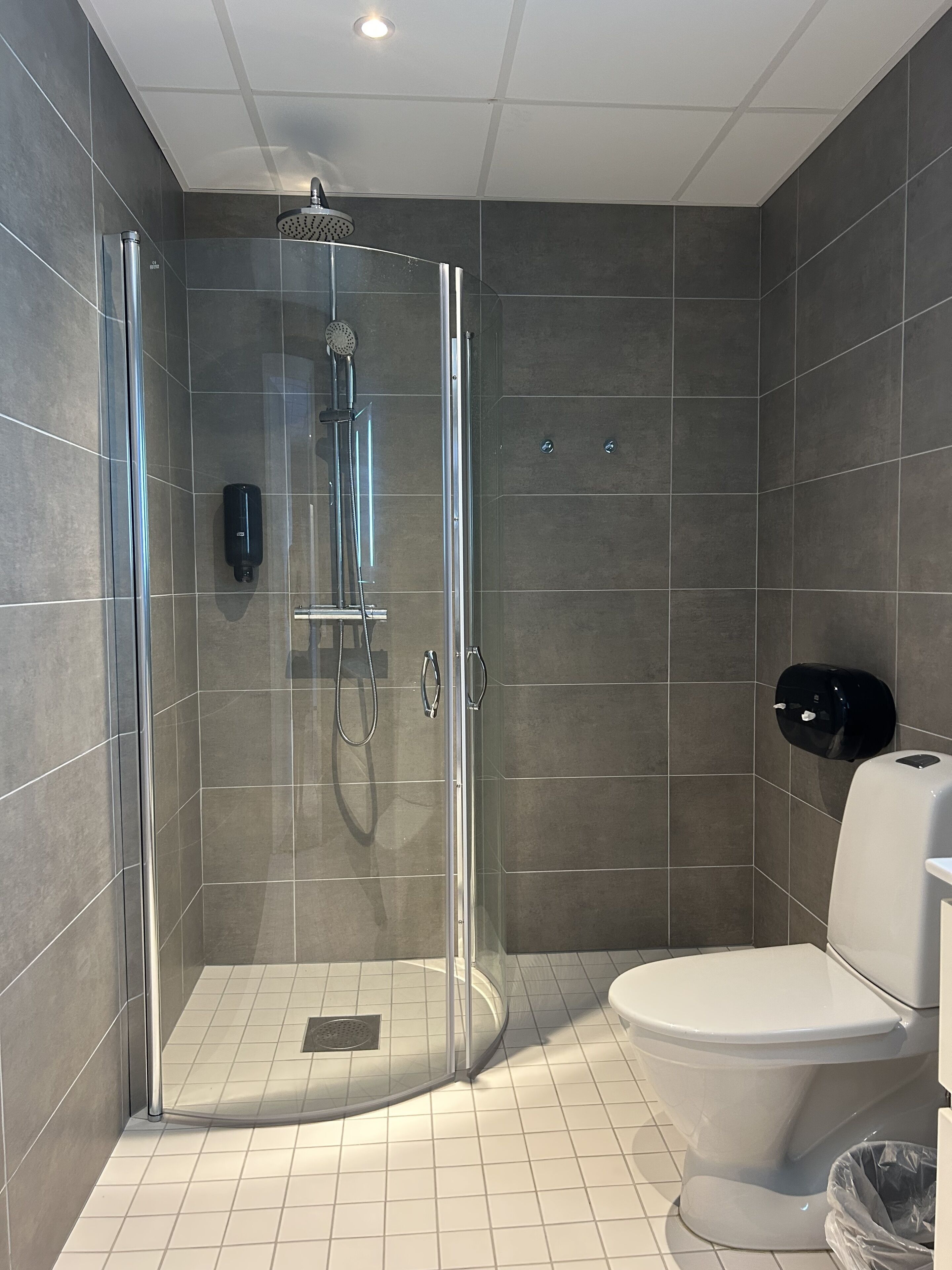 A modern bathroom with a glass-enclosed shower, a toilet, and a hand dryer.