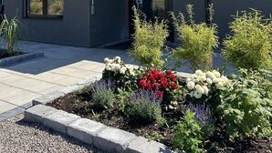A modern building with a dark facade, a glass balcony, and a small garden with various plants and flowers. - Hotell Solstickan Mellbystrand (Mellbystrand)