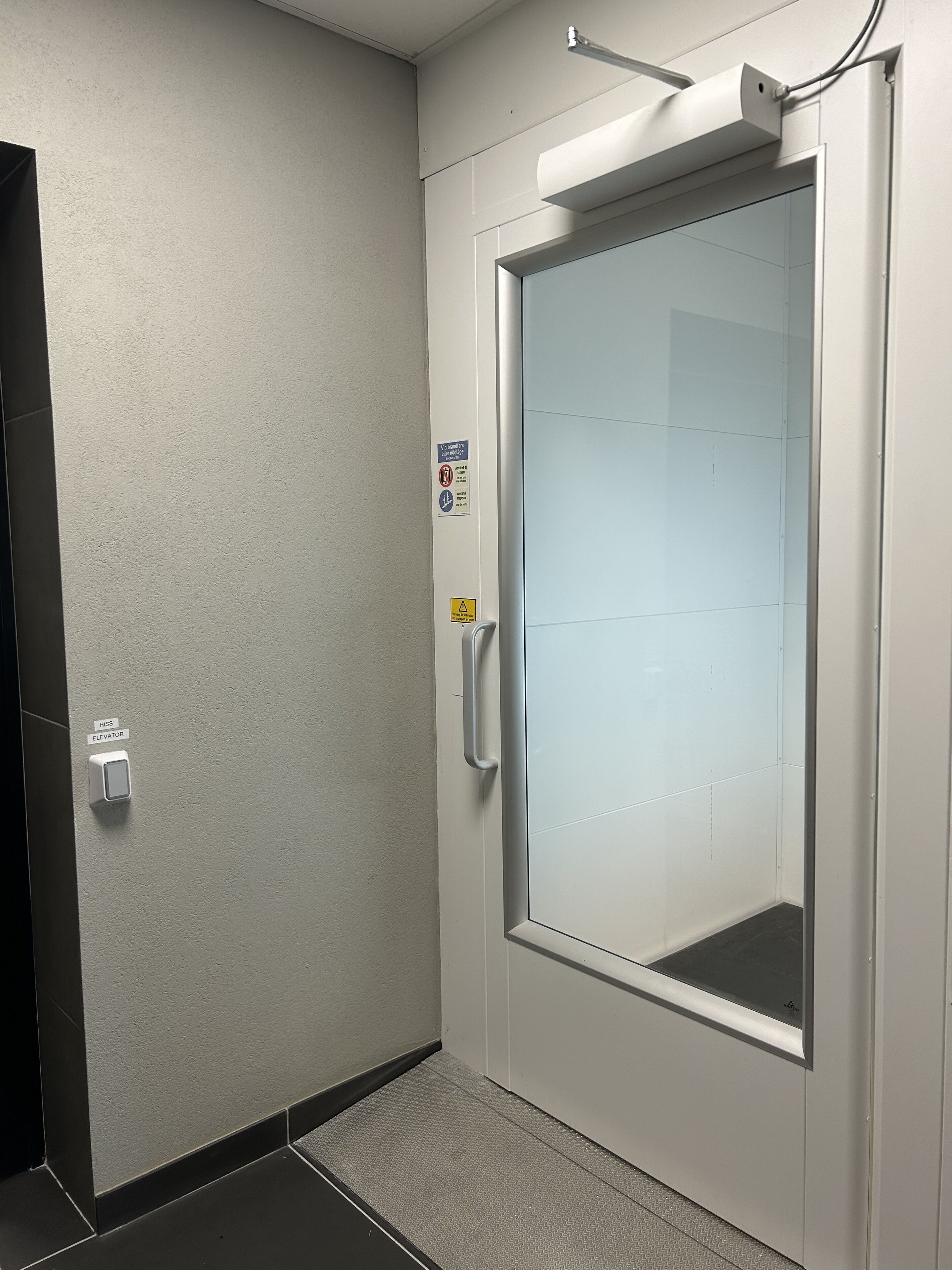 A modern elevator with a glass door, a handrail, and a control panel labeled "HISS ELEVATOR".
