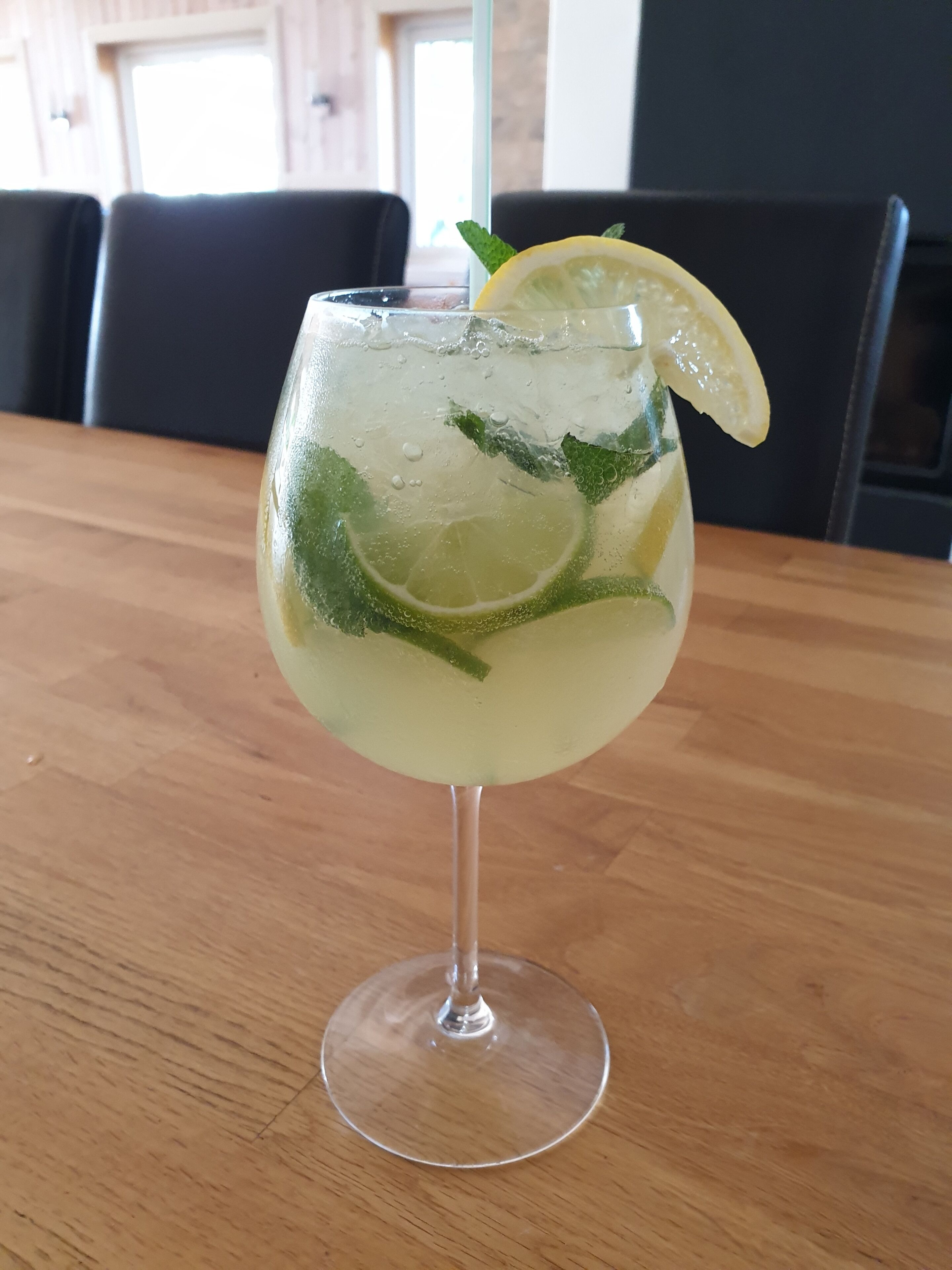 Un vaso de una bebida de color claro con una rodaja de limón y hojas de menta sobre una mesa de madera.