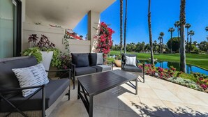 Une terrasse aménagée avec un canapé, des fauteuils et une table, offrant une vue sur un terrain de golf et un étang.