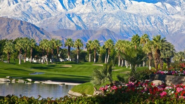 Un parcours de golf avec un étang, des palmiers et une chaîne de montagnes en arrière-plan.