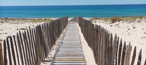 A wooden boardwalk leading to the beach, flanked by sand dunes and a wooden fence.