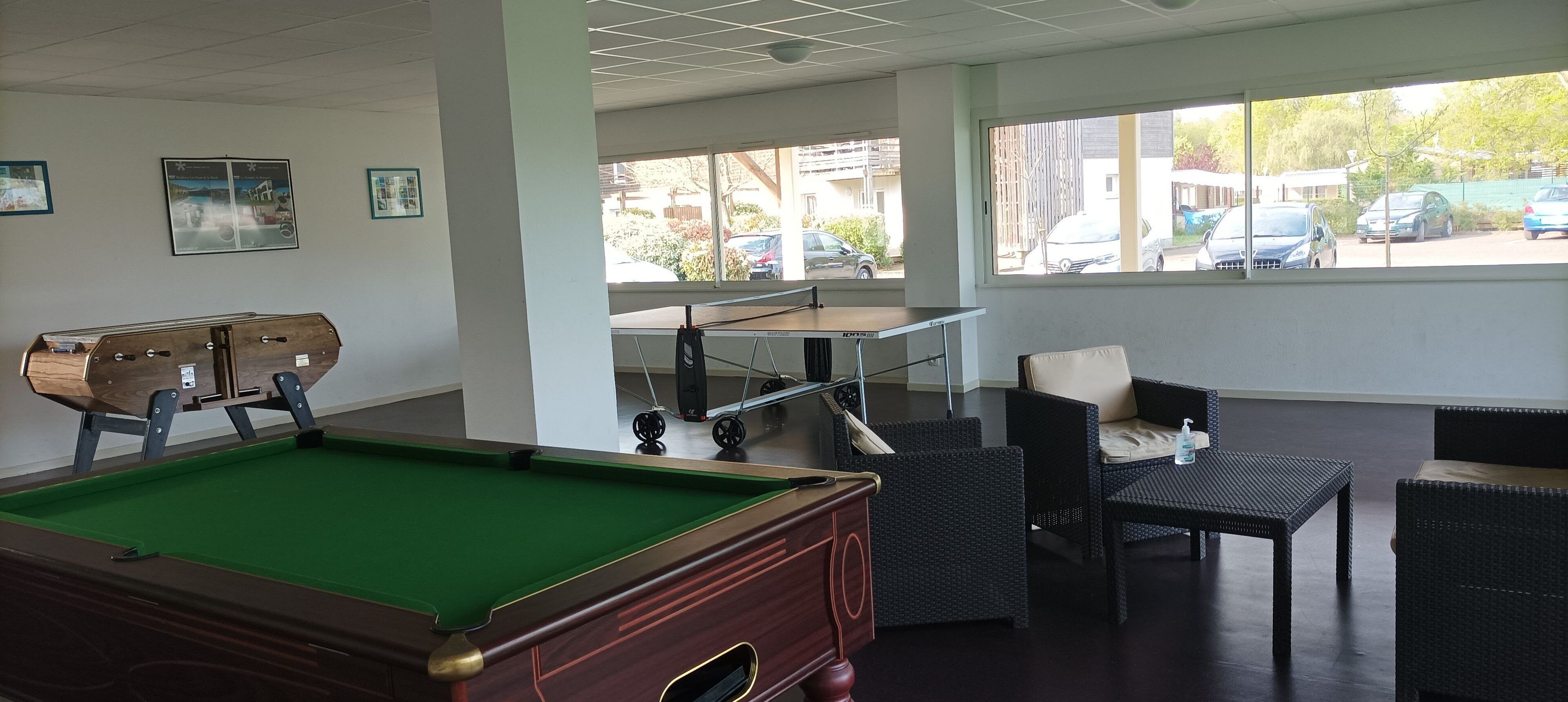 Une table de billard avec un meuble en bois, des meubles en osier et une vue sur les voitures garées à l’extérieur.