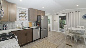 Una cucina moderna con elettrodomestici in acciaio inossidabile, mobili in legno e un'area pranzo con tavolo e sedie bianche.