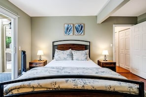 A bedroom with a bed, two bedside lamps, a wall-mounted heater, and two framed artworks.