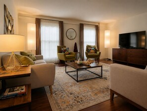 Ein Wohnzimmer mit Sofa, Sesseln, Couchtisch, Fernseher und Bücherregal.