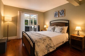 Un dormitorio con una cama, dos mesitas de noche, una lámpara de pie, una ventana con cortinas y dos obras de arte colgadas en la pared.